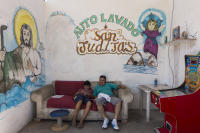 A father and son resting on sofa surrounded by religious murals at a car-wash.
 - © Viviane Moos